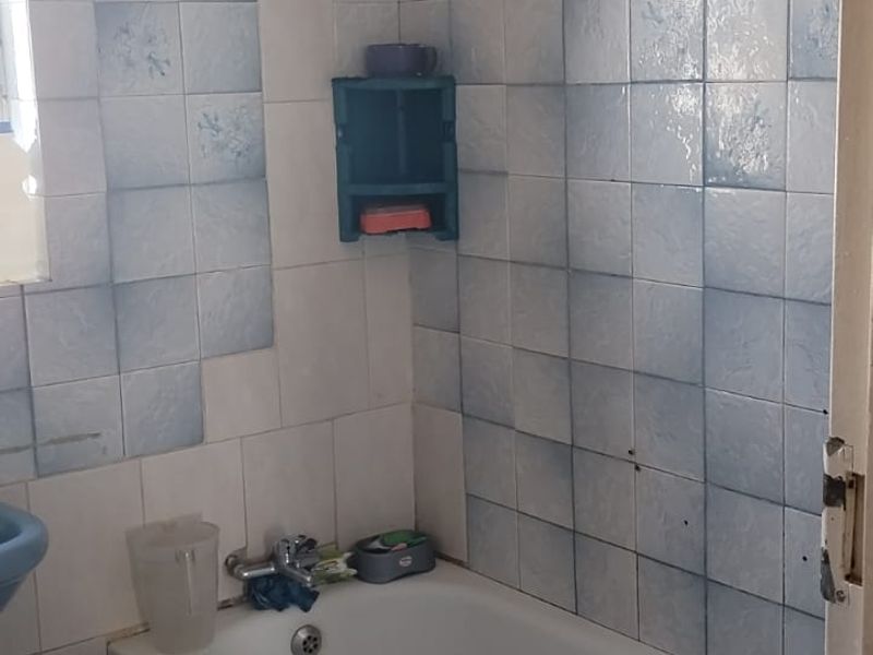 A dated bathroom featuring a standard bathtub with blue and white wall tiling and a shower curtain rod.