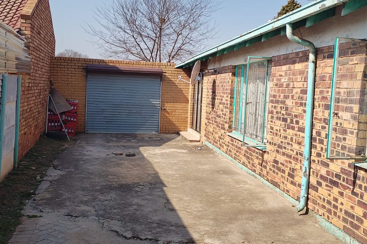 Rear exterior view of the property featuring a concrete driveway, brick facade, and a roller shutter garage door.