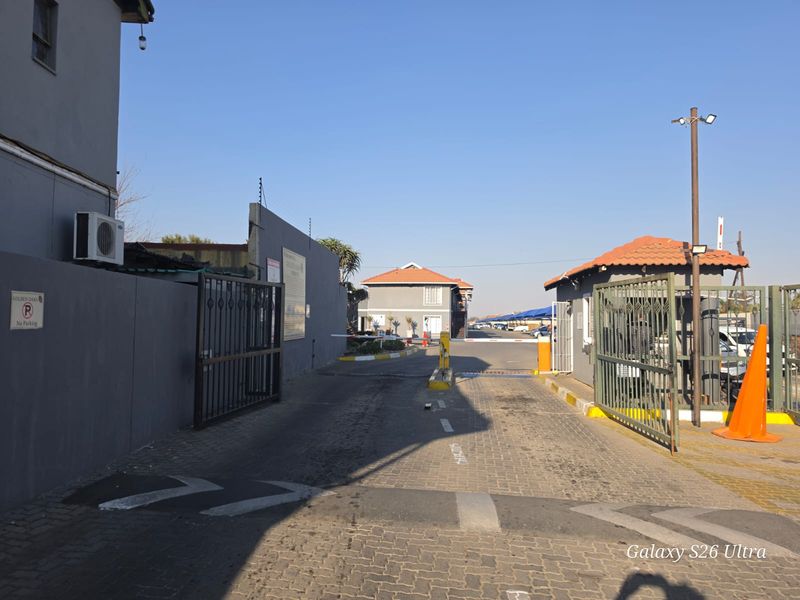 The entrance to the apartment complex features a secure boom gate, paved driveway, and perimeter wall with electric fencing for added security.