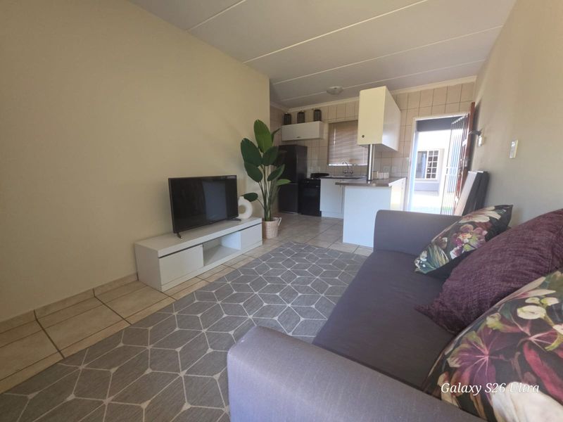 Open-plan living area featuring tiled flooring and a functional kitchen space with built-in cabinetry and direct access to the exterior.