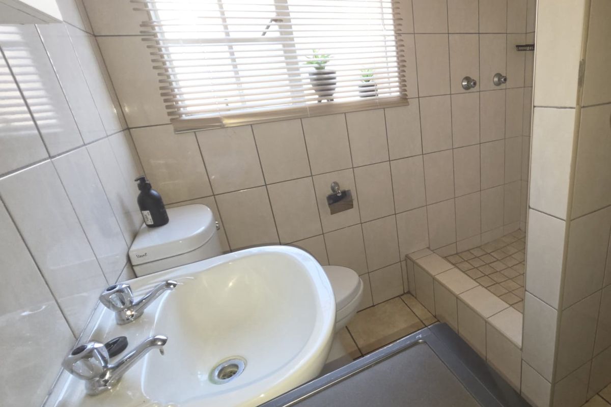 Compact bathroom featuring a pedestal basin, toilet, and a tiled shower cubicle with neutral wall tiling and natural light.