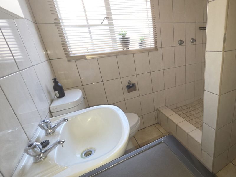 Compact bathroom featuring a pedestal basin, toilet, and a tiled shower cubicle with neutral wall tiling and natural light.