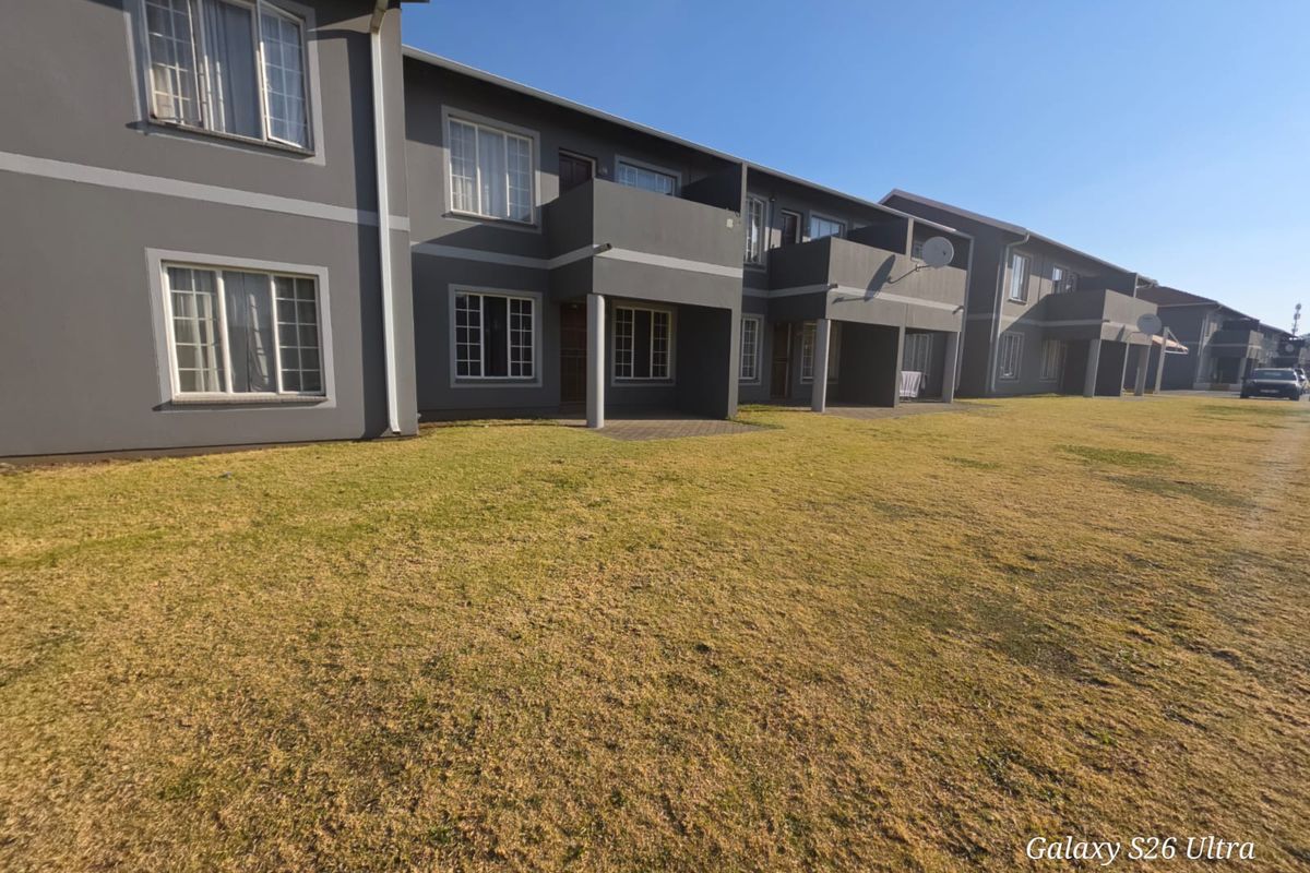 Exterior view of an apartment complex featuring ground floor patios, balconies, and a large communal lawn area.