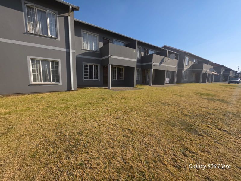 Exterior view of an apartment complex featuring ground floor patios, balconies, and a large communal lawn area.
