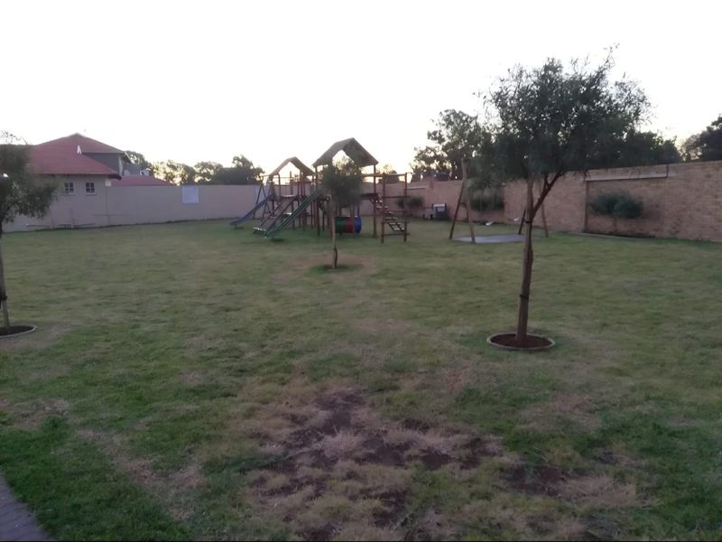 A spacious communal garden area featuring a lawn, perimeter boundary walls, and fixed playground equipment for residents.