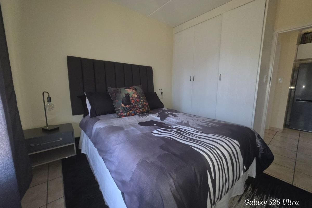 A compact bedroom featuring built-in wardrobes and tiled flooring, providing a functional sleeping space with direct access to the adjacent kitchen area.