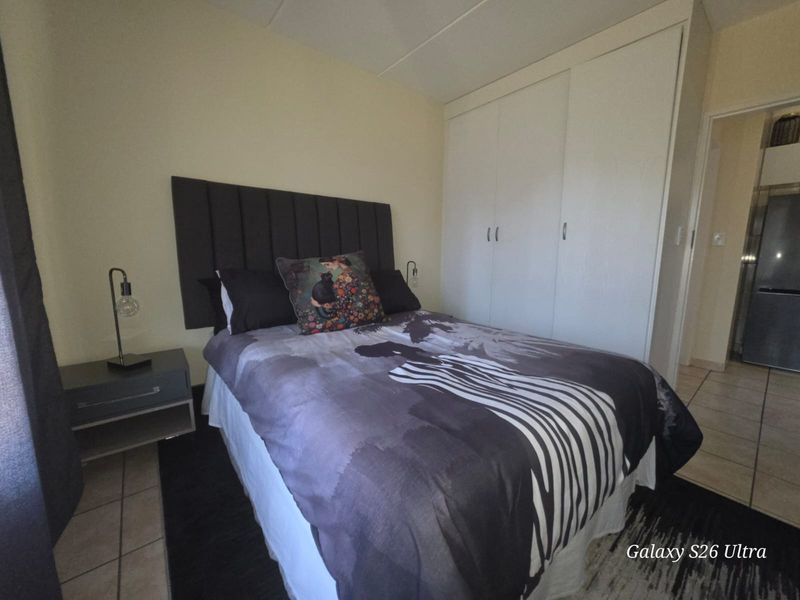 A compact bedroom featuring built-in wardrobes and tiled flooring, providing a functional sleeping space with direct access to the adjacent kitchen area.