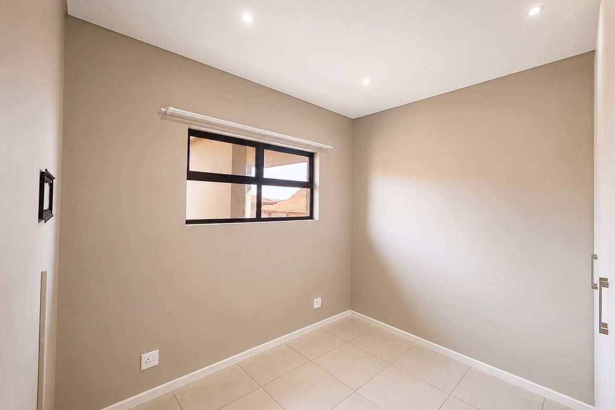 A clean, empty bedroom featuring neutral wall tones, tiled flooring, recessed downlights, and built-in cupboard storage.