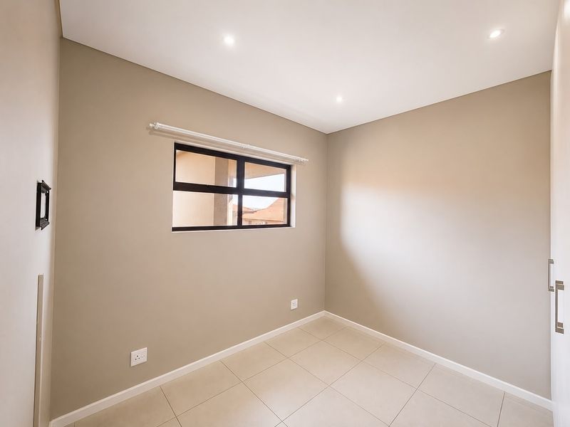 A clean, empty bedroom featuring neutral wall tones, tiled flooring, recessed downlights, and built-in cupboard storage.