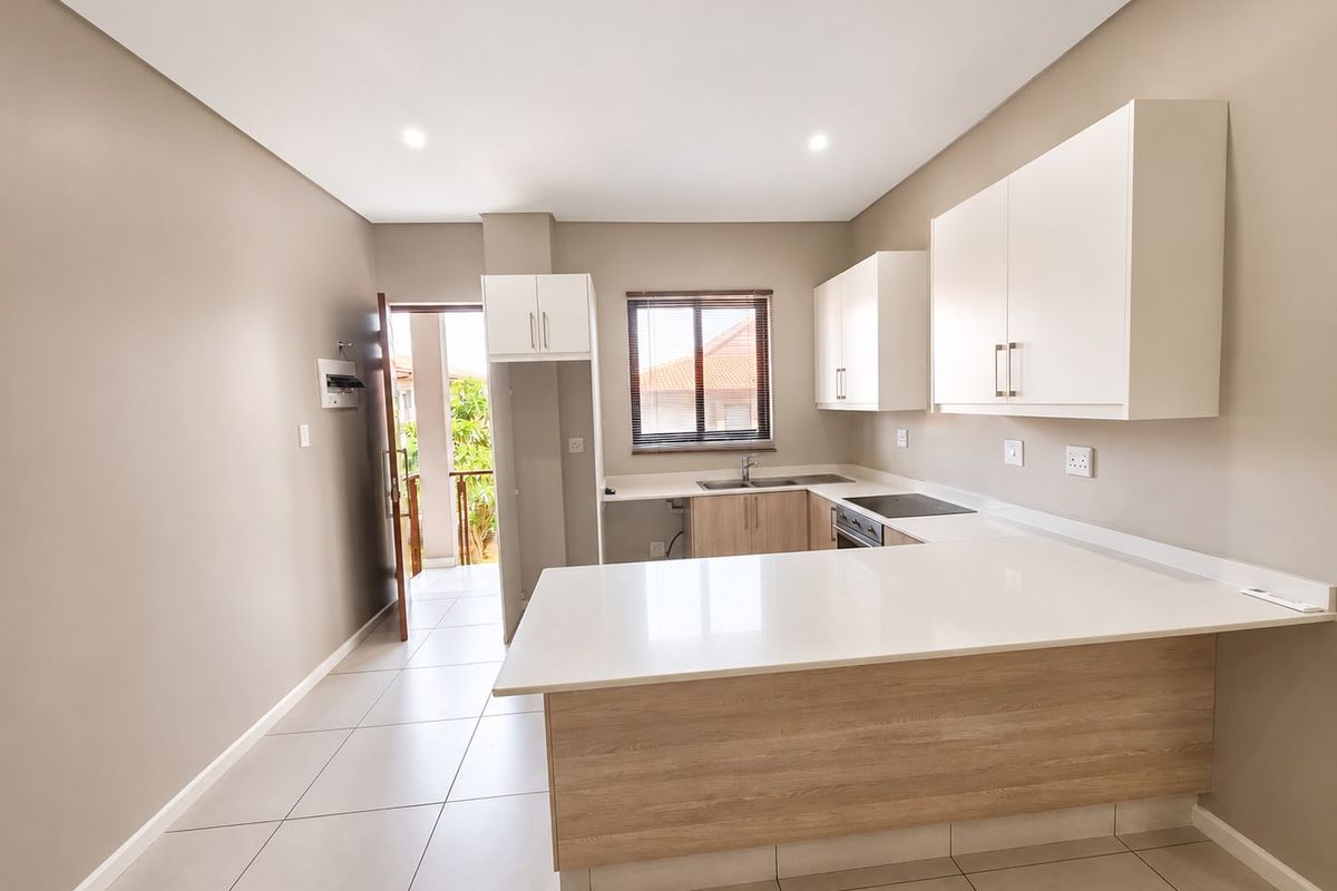 Modern kitchen featuring white cabinetry, quartz countertops, an electric hob, and tiled flooring, with direct access to an outdoor balcony area.