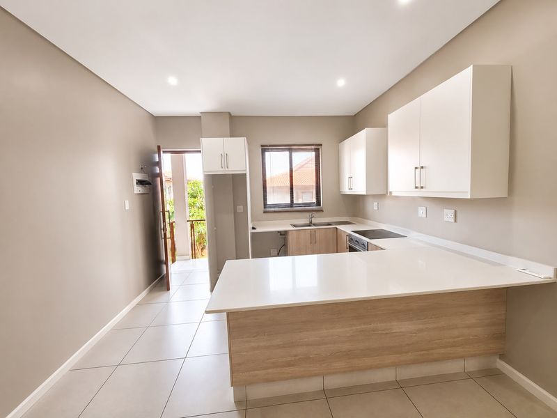 Modern kitchen featuring white cabinetry, quartz countertops, an electric hob, and tiled flooring, with direct access to an outdoor balcony area.