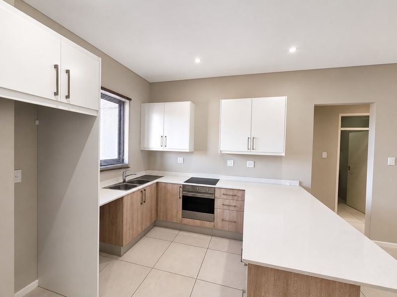 Modern kitchen featuring light wood-finish cabinetry, white stone countertops, integrated electric hob and oven, and neutral tiled flooring.