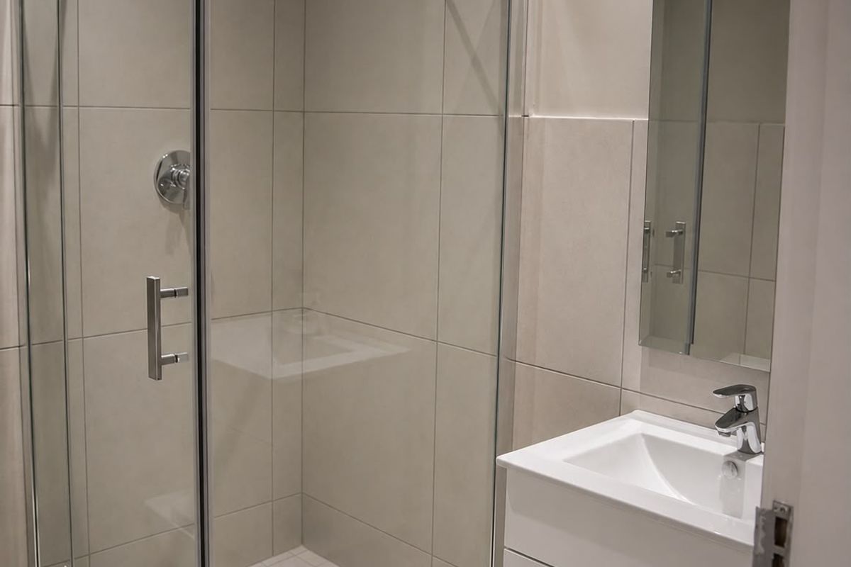 Modern bathroom featuring a glass-enclosed shower, a sleek vanity with integrated basin, and neutral wall tiling.