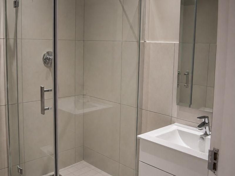 Modern bathroom featuring a glass-enclosed shower, a sleek vanity with integrated basin, and neutral wall tiling.
