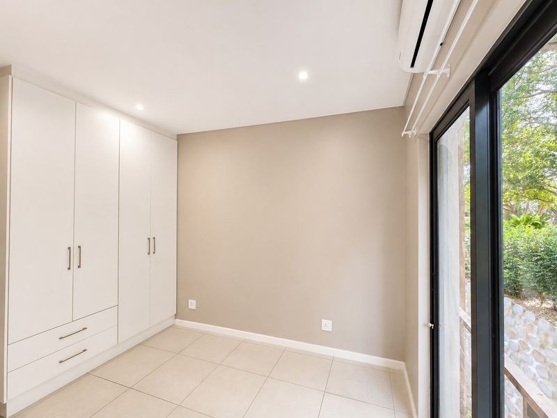 A bright, empty bedroom featuring modern built-in cupboards, tiled flooring, and a sliding glass door providing access to the outdoors.