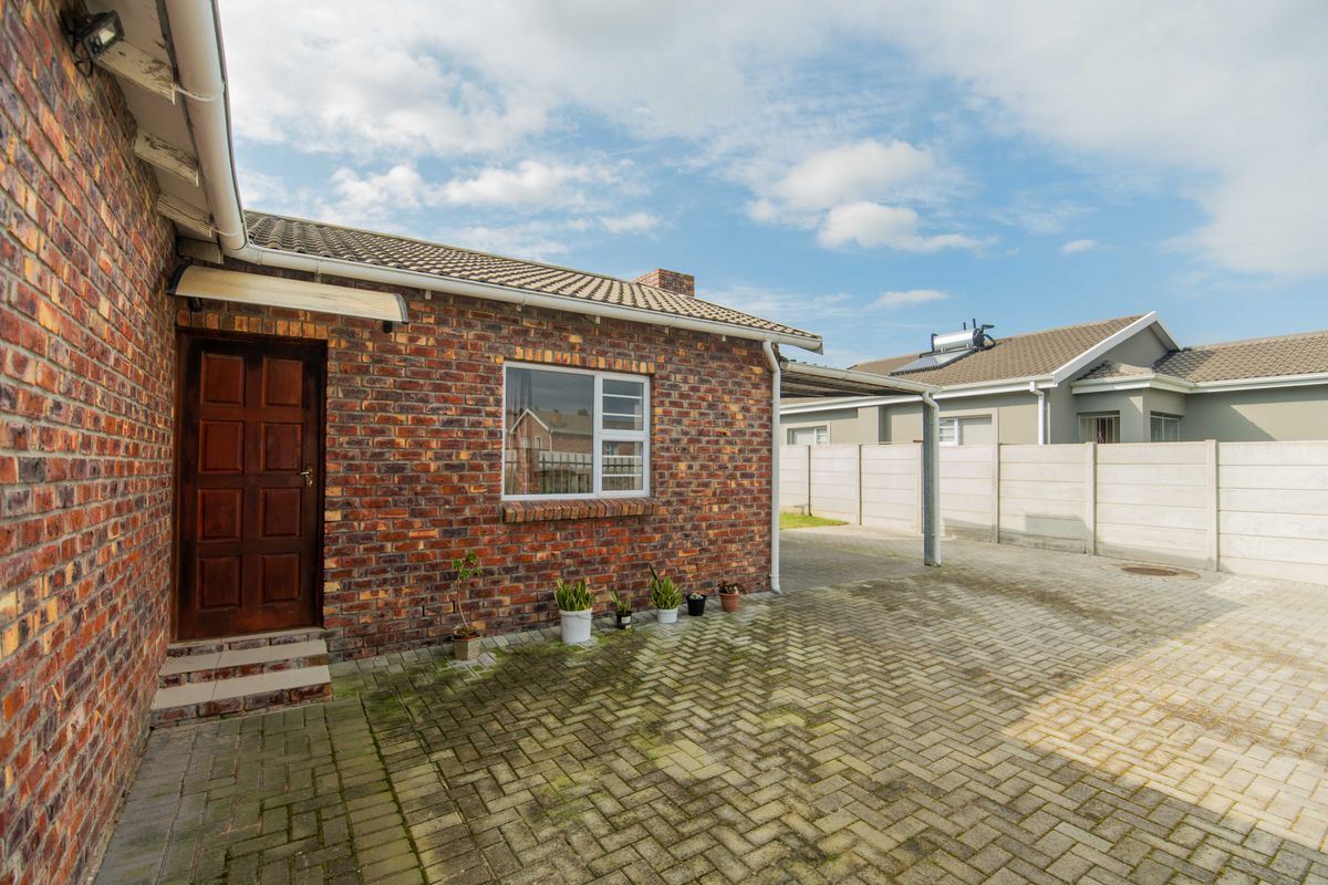 Rear exterior view featuring a face brick facade, paved driveway, carport, and precast concrete boundary wall.