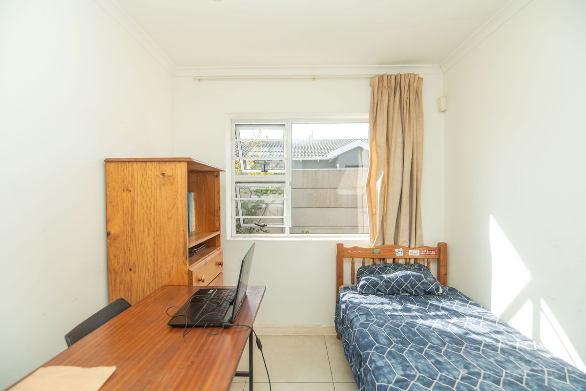 A compact bedroom featuring tiled flooring, neutral walls, and an aluminium-framed window providing natural light.