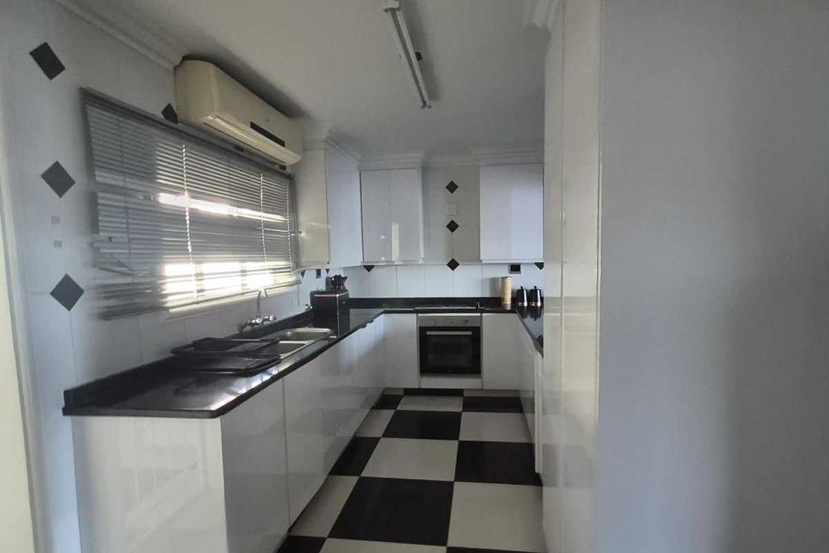 A functional kitchen featuring high-gloss white cabinetry, black granite countertops, and a distinctive black and white checkered floor.