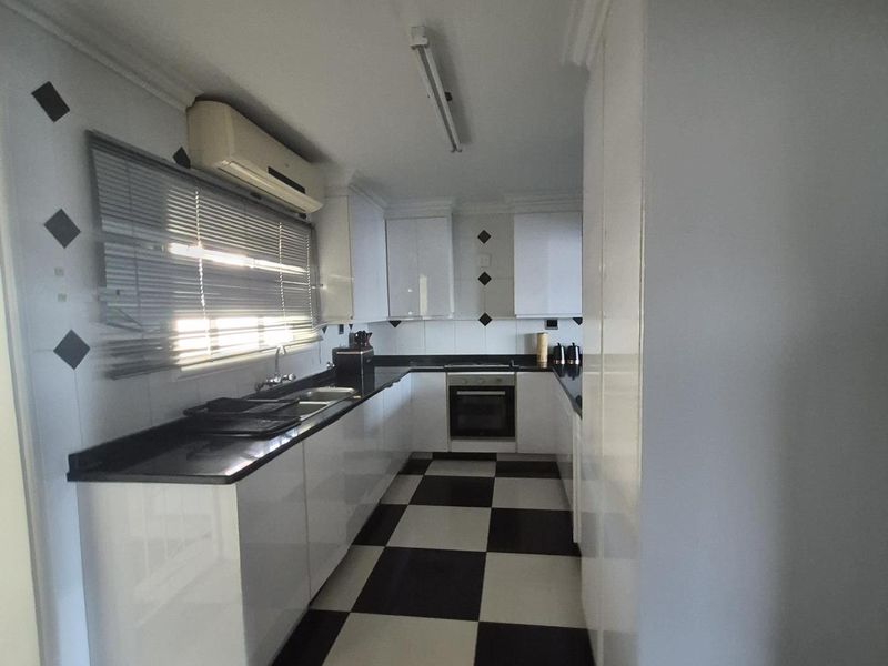 A functional kitchen featuring high-gloss white cabinetry, black granite countertops, and a distinctive black and white checkered floor.