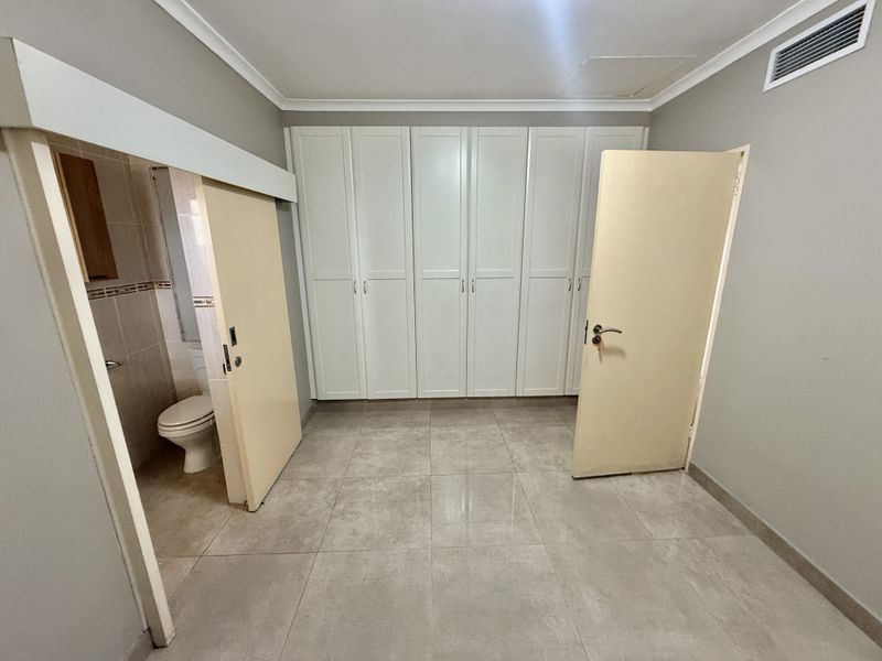 A spacious bedroom featuring neutral tiled flooring, extensive built-in cabinetry, and direct access to an en-suite bathroom.