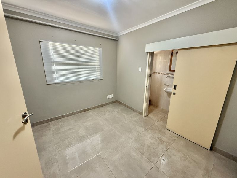 An empty bedroom featuring tiled flooring, a sliding door leading to an en-suite bathroom, and venetian blinds.