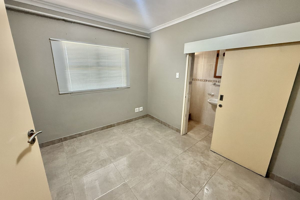 An empty bedroom featuring tiled flooring, a sliding door leading to an en-suite bathroom, and venetian blinds.