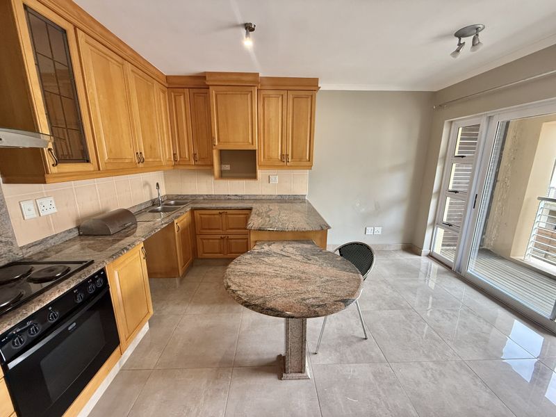 A functional kitchen featuring wooden cabinetry, granite countertops, a built-in oven, and tiled flooring, with direct access to an outdoor balcony area.