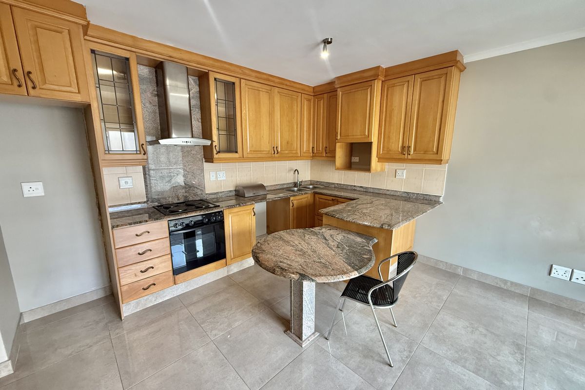 A functional kitchen featuring wooden cabinetry, granite countertops, a built-in oven, hob, extractor fan, and tiled flooring.