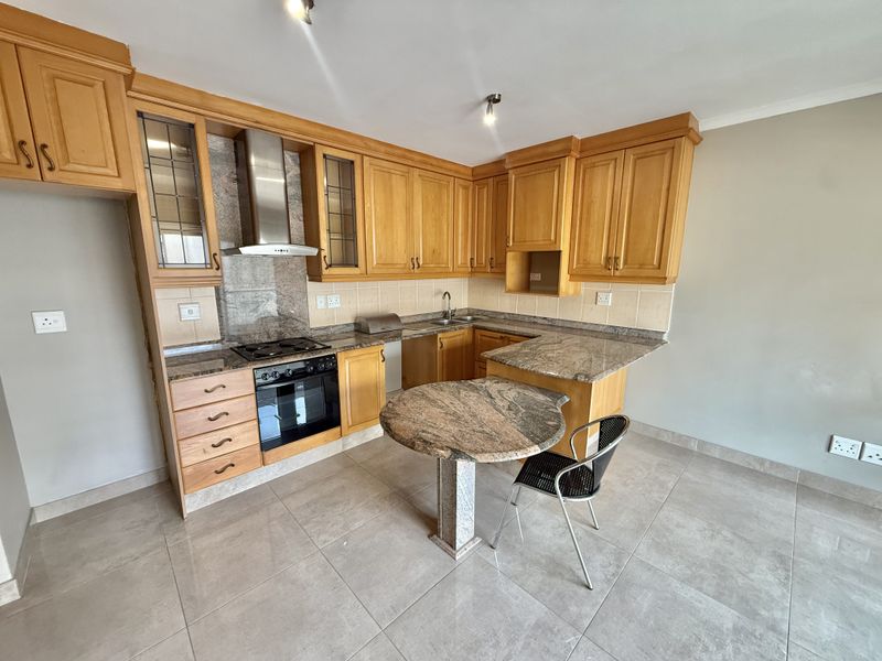 A functional kitchen featuring wooden cabinetry, granite countertops, a built-in oven, hob, extractor fan, and tiled flooring.