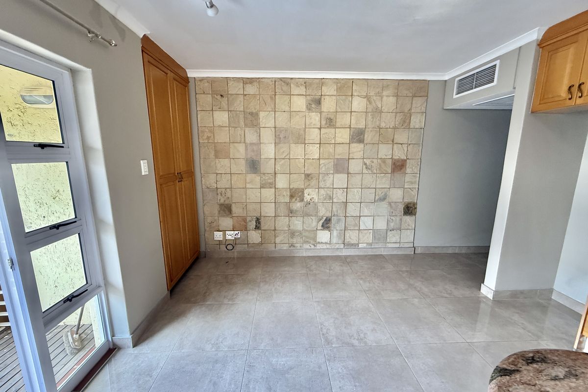 An open-plan living area featuring large floor tiles, a decorative stone feature wall, built-in cabinetry, and direct access to an outdoor patio area.