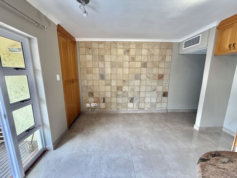 An open-plan living area featuring large floor tiles, a decorative stone feature wall, built-in cabinetry, and direct access to an outdoor patio area.
