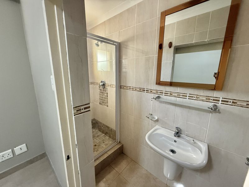 A functional bathroom featuring a pedestal basin, a shower enclosure with tiled accents, and neutral wall tiling throughout.