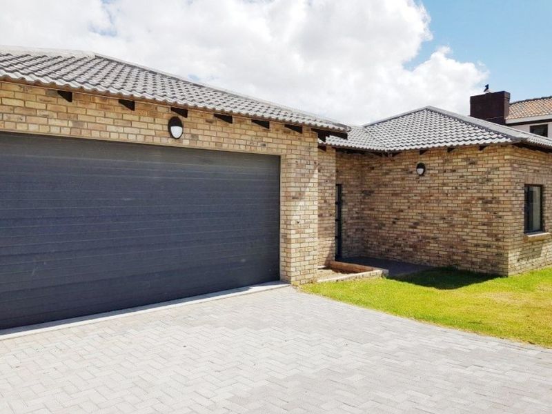 Front view of the property featuring a brick facade, tiled roof, and a paved driveway leading to a modern sectional garage door.
