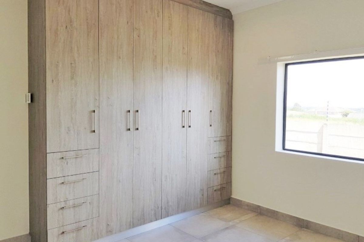 A bright, empty bedroom featuring modern light wood-grain built-in cupboards and neutral floor tiles.