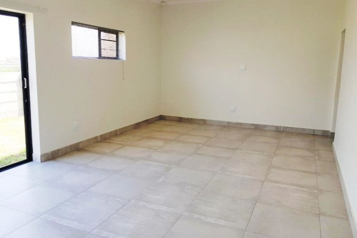 A bright, empty living area featuring neutral tiled flooring, recessed lighting, and a sliding glass door providing access to the exterior.
