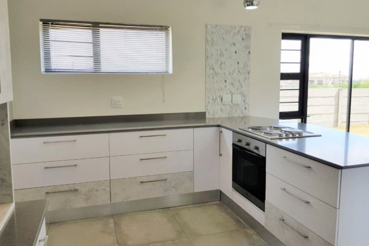 Modern kitchen featuring white cabinetry, stone countertops, built-in oven, gas hob, and tiled flooring with direct access to the outdoor area.