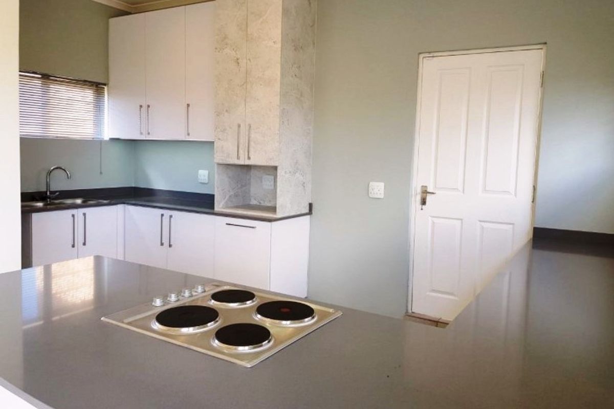 A clean, modern kitchen featuring white cabinetry, stone-look accents, a central island with an integrated electric hob, and a functional sink area.