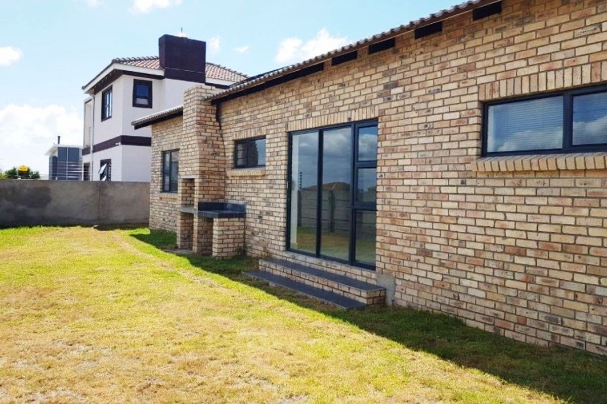 Rear view of a face brick house featuring a built-in braai, sliding glass doors, and a small garden area.