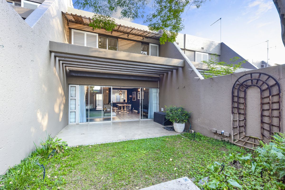 Rear view of the townhouse featuring a covered patio, sliding glass doors leading to the interior, and a private garden area with a trellis.