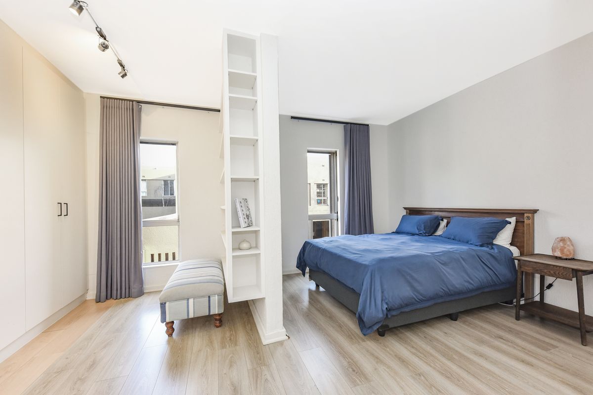 Spacious bedroom featuring modern laminate flooring, a built-in wardrobe, and a functional room-dividing shelving unit with integrated track lighting.