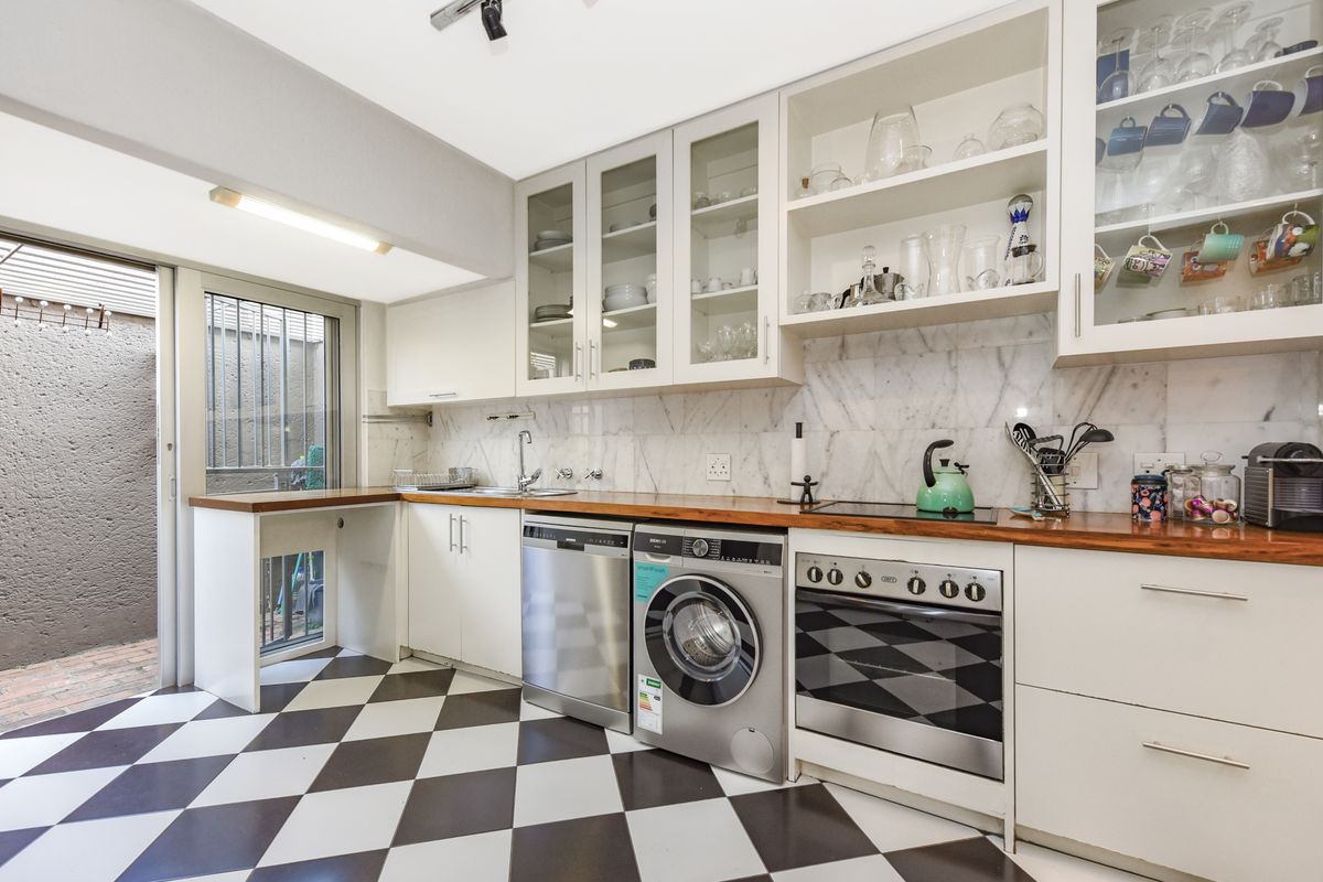 A well-appointed kitchen featuring white cabinetry, marble backsplash, wooden countertops, and a classic checkered floor, with direct access to an outdoor area.