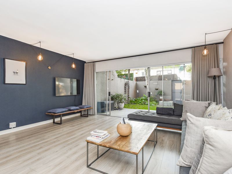 A bright living room featuring laminate flooring, a dark accent wall, and large sliding glass doors that open onto a private rear courtyard.