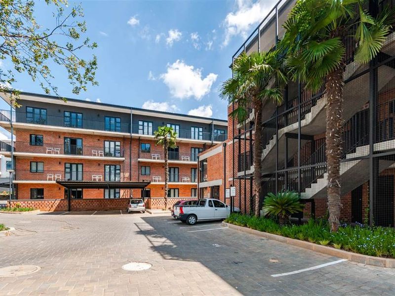 A well-maintained apartment complex exterior featuring brick facade, paved parking area, and external staircases with modern metal railings.