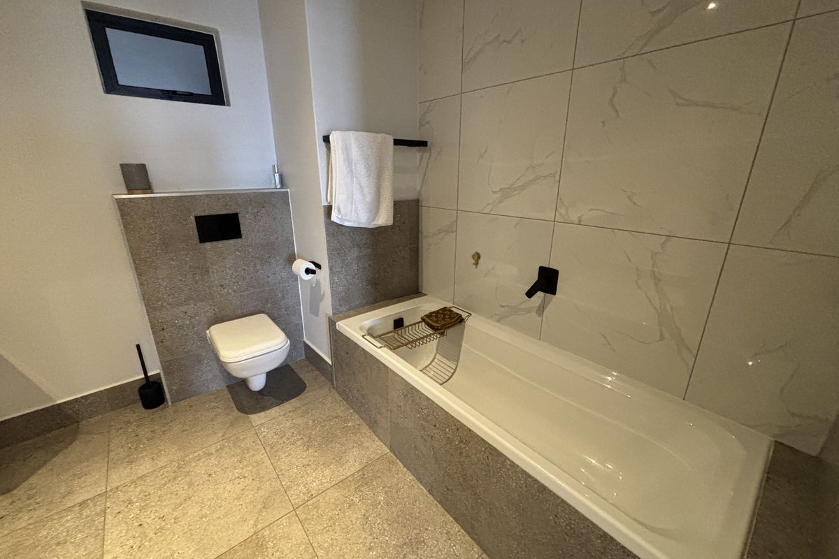 Modern bathroom featuring a wall-mounted toilet, built-in bathtub with wall-mounted fixtures, and contemporary large-format marble-look wall tiles.
