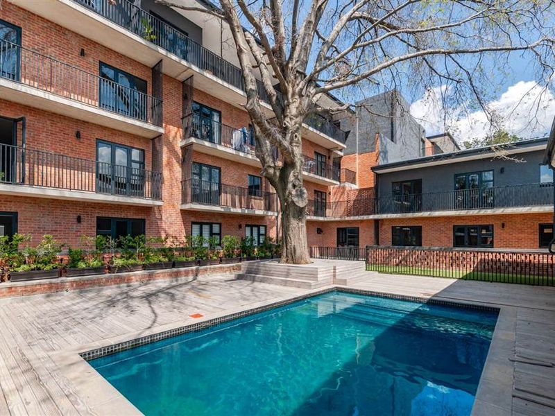 A well-maintained apartment complex courtyard featuring a swimming pool, timber decking, and exposed brick architecture with private balconies.