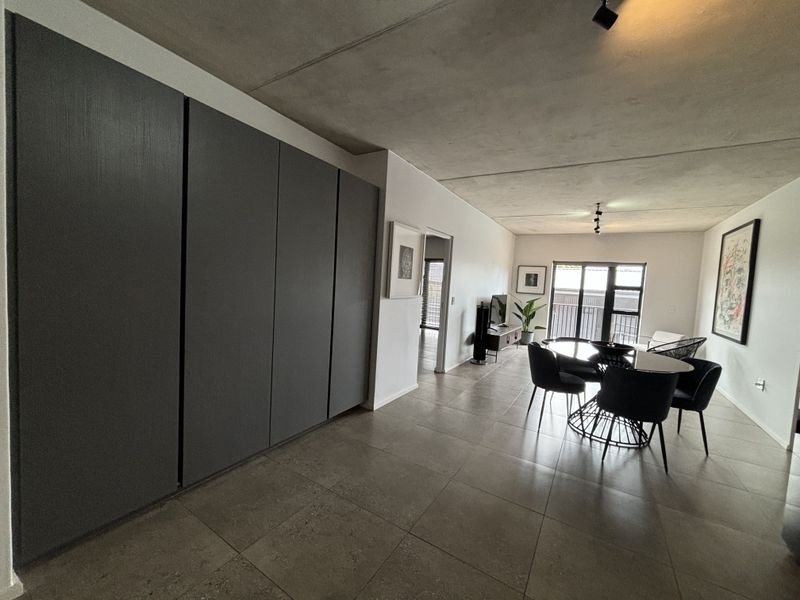 Spacious open-plan living and dining area featuring modern tiled floors, exposed concrete ceilings, and extensive built-in cabinetry with access to a balcony.