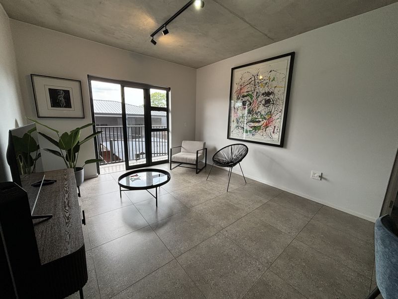 Modern living room featuring an exposed concrete ceiling, track lighting, large format floor tiles, and direct access to a private balcony.