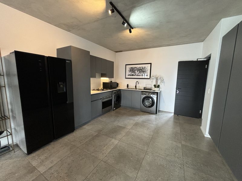 Modern kitchen featuring dark grey cabinetry, integrated appliances, gas hob, oven, and sleek tiled flooring under an exposed concrete ceiling.