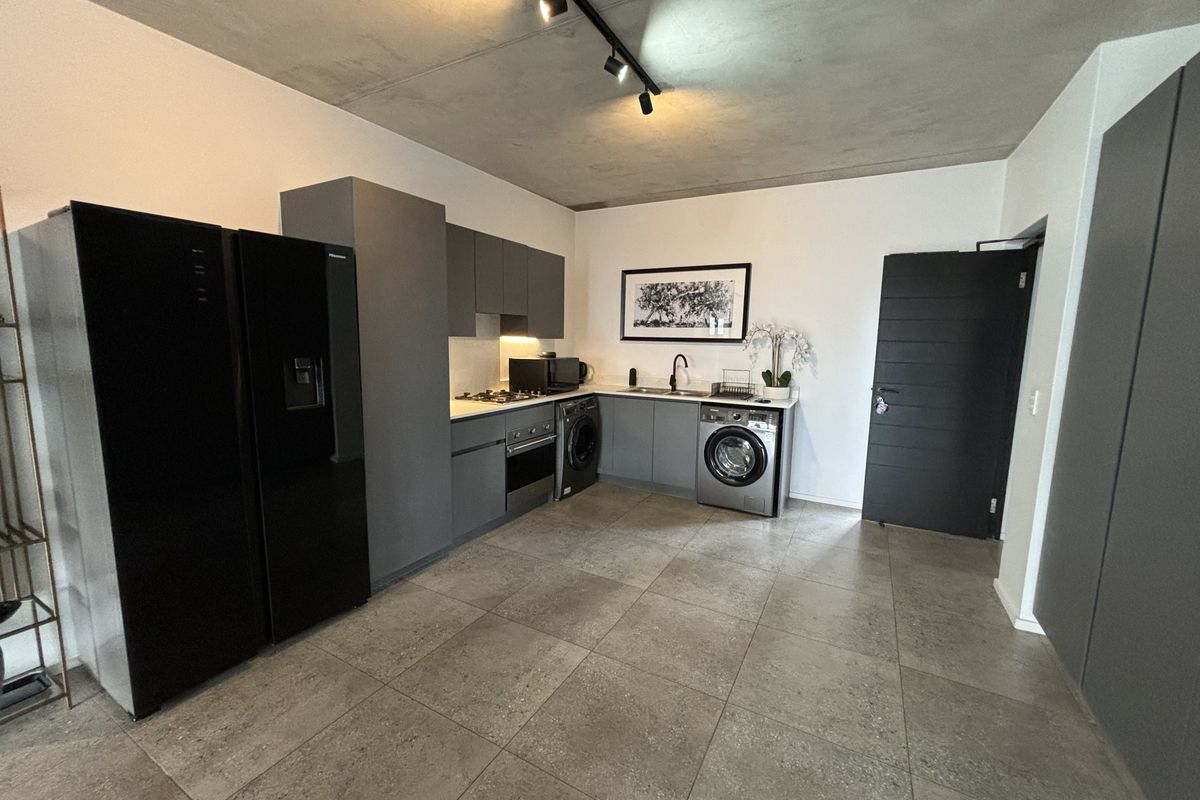 Modern kitchen featuring dark grey cabinetry, integrated appliances, gas hob, oven, and sleek tiled flooring under an exposed concrete ceiling.