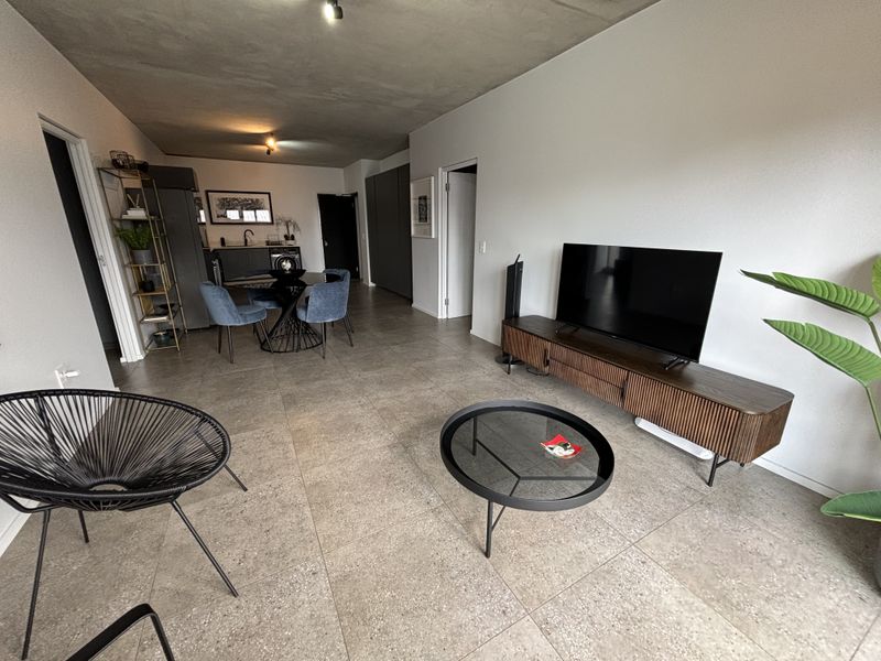 An open-plan living and dining area featuring modern tiled flooring, an exposed concrete ceiling, and integrated cabinetry, creating a contemporary and functional living space.